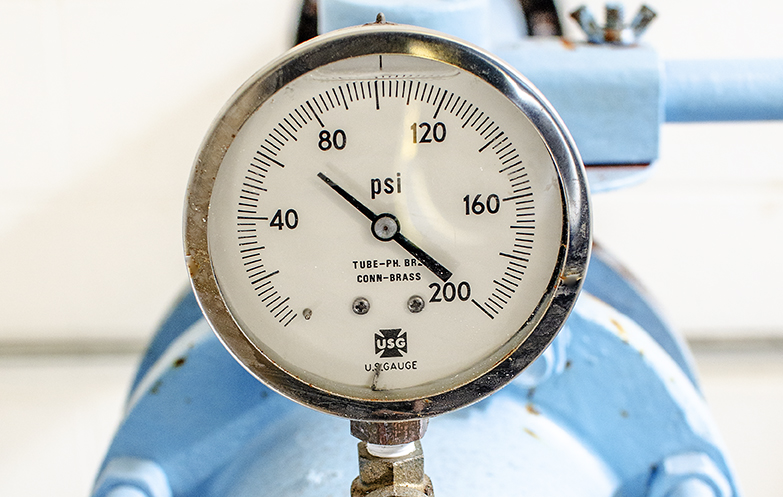 Fluid-filled pressure gauge on large water pipe showing 62psi